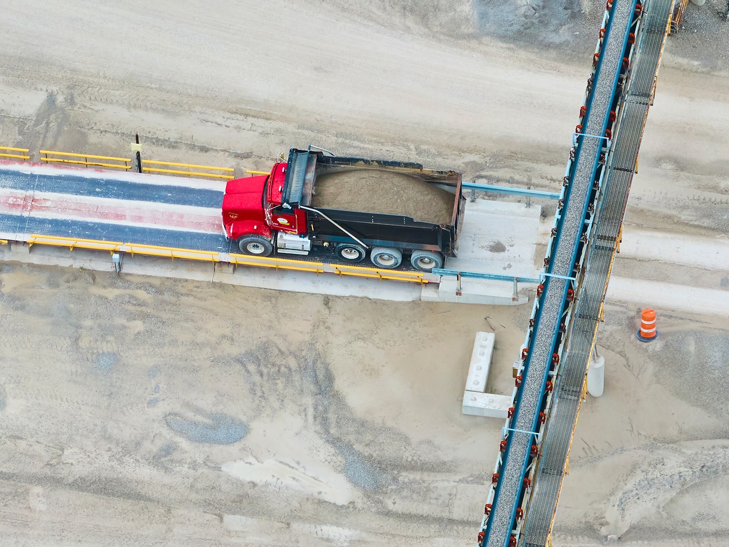 Aerial view of a haul truck on a weighbridge beside a conveyor at a resource recovery facility