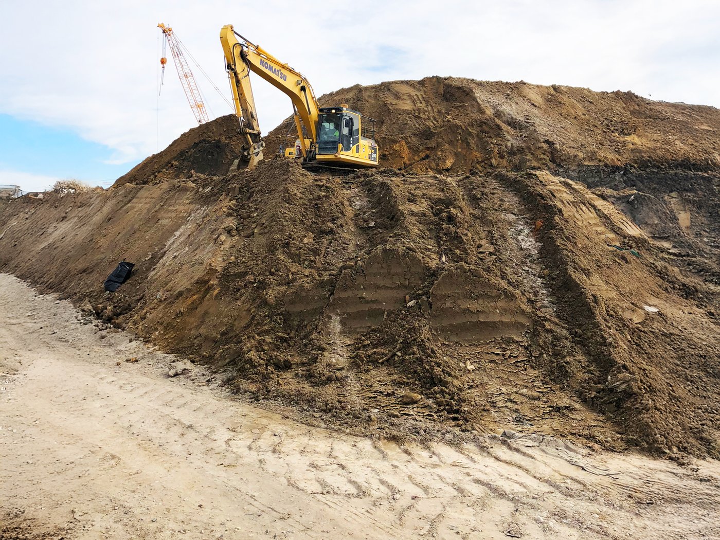 An excavator working a large soil stockpile on a greenfield earthworks site